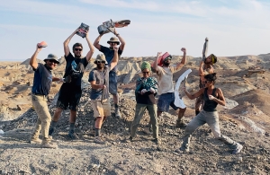 a group of paleontologists pose with tools on in a desert setting